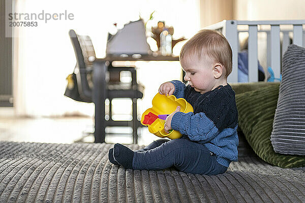 Baby spielt auf dem Bett  während seine Mutter sich fertig macht und Spaß mit neuen Spielsachen hat. Entdecken und lernen