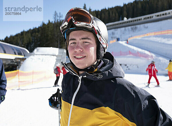 Junger attraktiver Mann in Skiausrüstung am Fuße einer Piste. glücklich und lächelnd