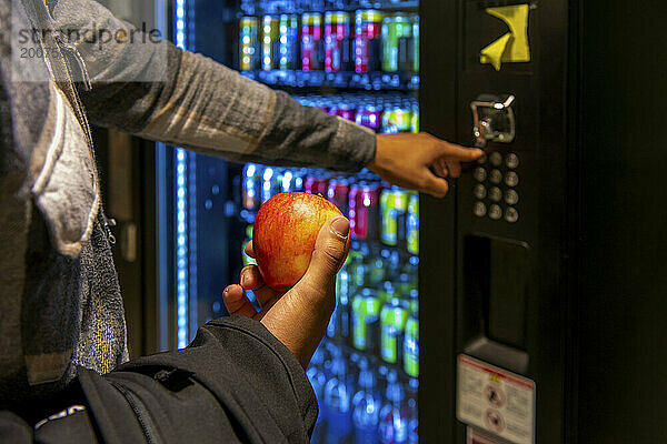 Student eating an apple putting money into a vending machine