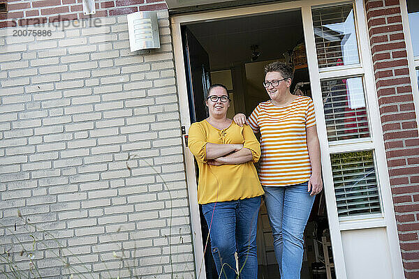 Gleichgeschlechtliches Paar steht glücklich in der Tür seines Hauses und berührt sich