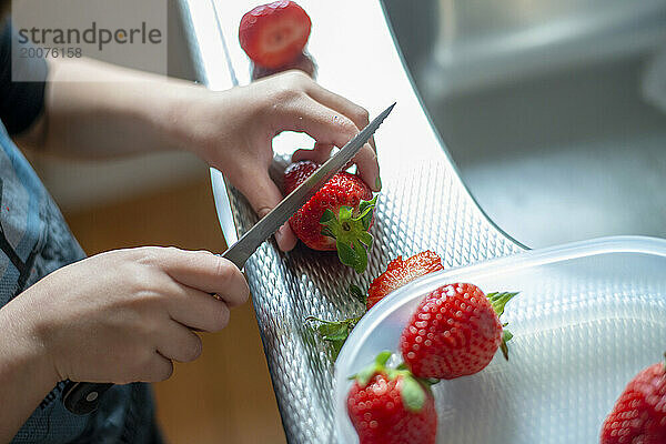 Kleiner Junge schneidet mit Hilfe seiner Mutter gesunde Erdbeeren