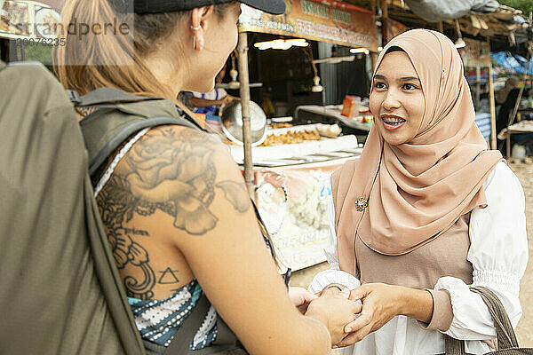 Zwei junge Frauen  eine davon trägt einen Hijab  begrüßen einander in einer ländlichen Stadt in Thailand