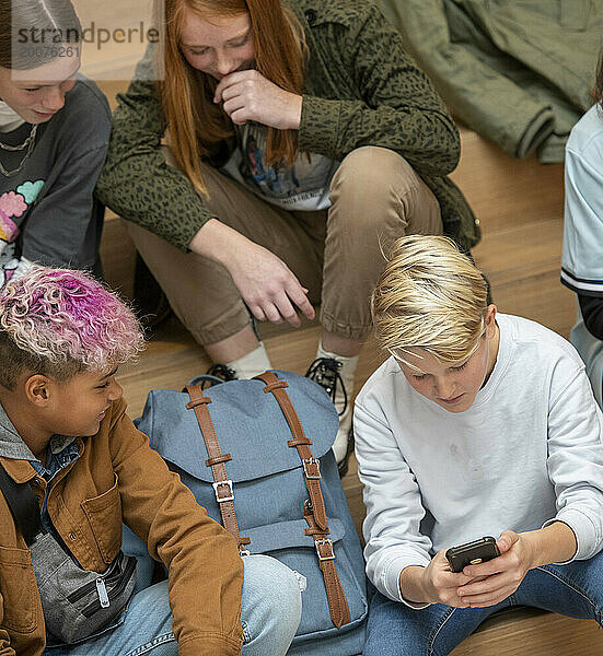 Gruppe junger Teenager  die in der Schule Kontakte knüpfen  während sie auf ihre Telefone schauen