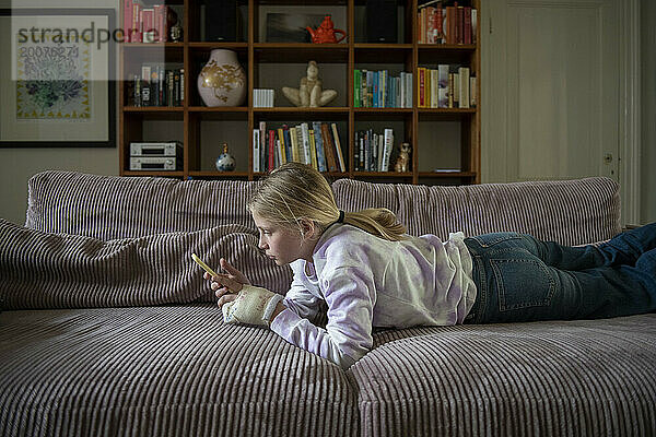Junger Teenager entspannt sich auf dem Sofa und recherchiert mit ihrem Telefon