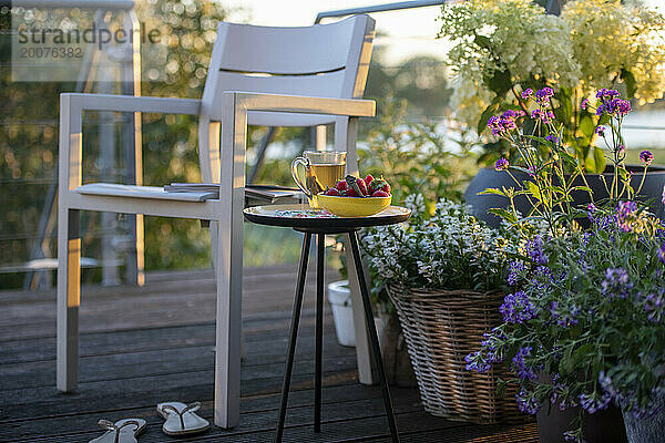 Frühstück mit Tee und Erdbeeren auf einem schönen Tisch in der Sommersonne. Garten und Kräuter in voller Blüte  Blumen.