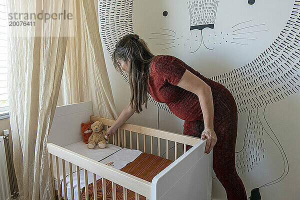 Schwangere Mutter arrangiert Teddys für ihr neues Baby im Kinderbett