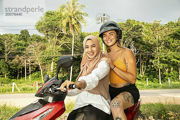 Porträt zweier junger Freundinnen  von denen eine einen Hijab trägt und ihr Moped anhält  um den Blick auf die Küste zu genießen