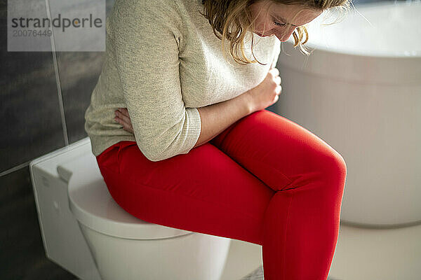 Frau sitzt mit Kopfschmerzen und Krämpfen aufgrund ihrer monatlichen Menstruation auf der Toilette. Kopf in ihrem Schoß mit gesundheitlichen Schmerzen