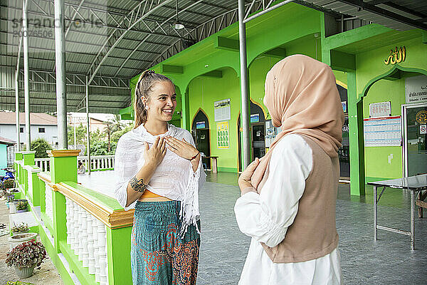 Zwei junge Freundinnen  eine davon trägt einen Hijab  zeigt ihrer Freundin  wie muslimische Frauen einander begrüßen.