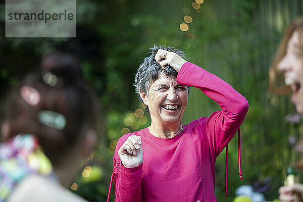 Eine reife Frau lacht mit Freunden und Familie auf einer Sommergartenparty