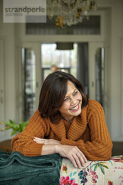 Attraktives Porträt einer älteren Frau  die sich zu Hause lachend auf Limonade stützt