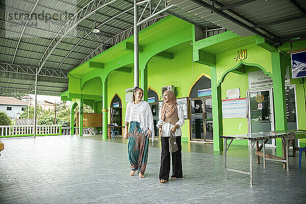 Zwei junge Frauen  eine davon trägt einen Hijab  führt ihre Freundin durch ihre Moschee