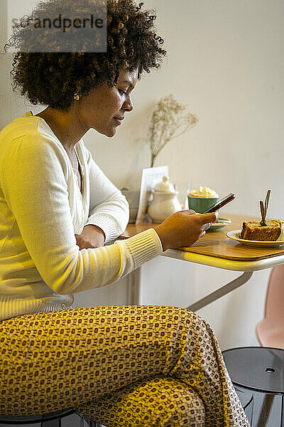 Attraktive Afrikanerin mit schönen Haaren sitzt mit ihrem Telefon in einem Café