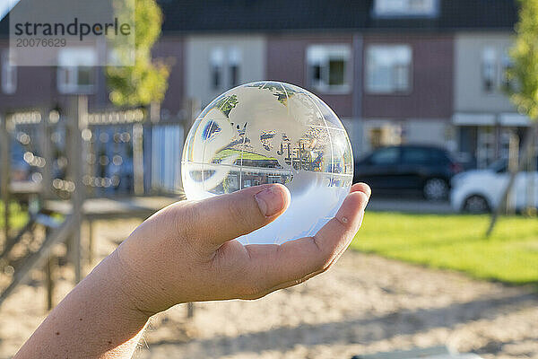 Kind hält eine Glaskugel in einem öffentlichen Park  reflektierendes Licht und klares Glas