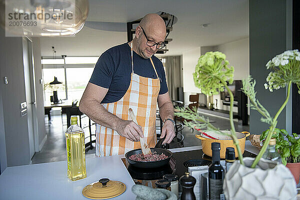 Erwachsener Mann bereitet in seiner modernen Küche Hackfleisch für eine Lasagne zu