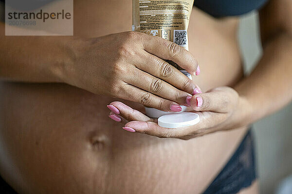 Schwangere Mutter trägt Creme auf ihren Bauch auf