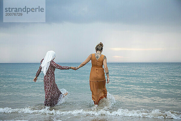 Zwei junge Frauen  beste Freundinnen  eine trägt einen Hijab  hat Spaß und genießt die Zeit am Strand.