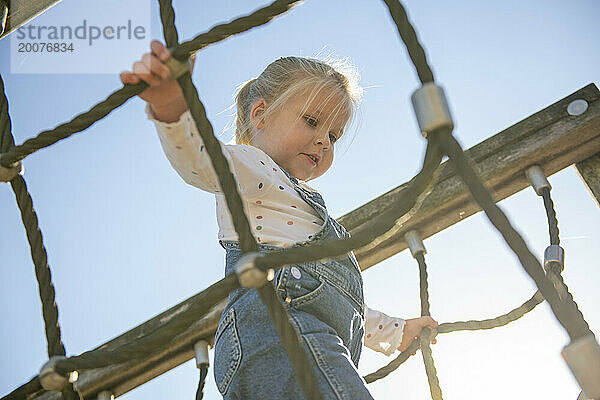 Kleines Mädchen klettert mutig durch einen Abenteuerspielplatz im öffentlichen Park