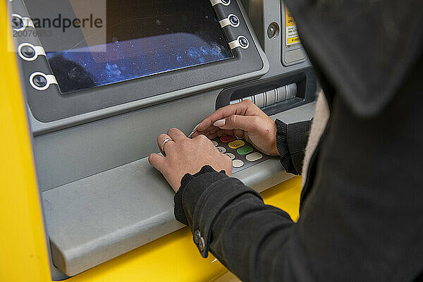 Junge Frau holt Geld aus ihrem Geldautomaten  der Geldautomat verdeckt aus Sicherheitsgründen ihre PIN