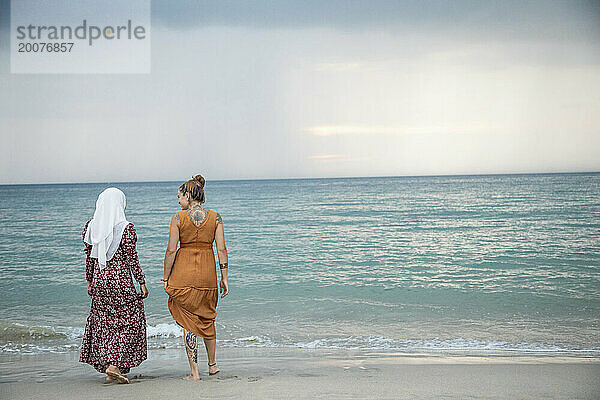 Zwei junge Frauen  beste Freundinnen  eine trägt einen Hijab  hat Spaß und genießt die Zeit am Strand.