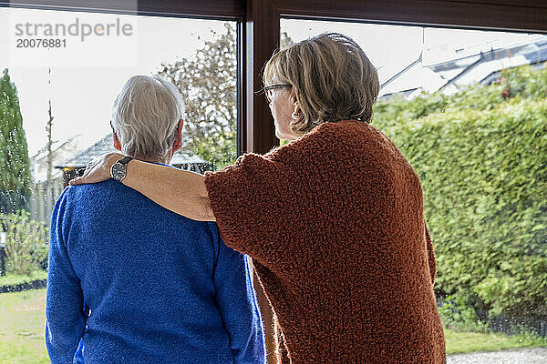 Zwei ältere Freunde stehen da und schauen aus dem Fenster und trösten sich gegenseitig