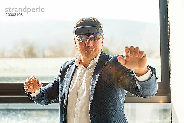 Frontalansicht eines Geschäftsmannes  der eine Mixed Reality Brille trägt und einen interaktiven Bildschirm im Büro berührt