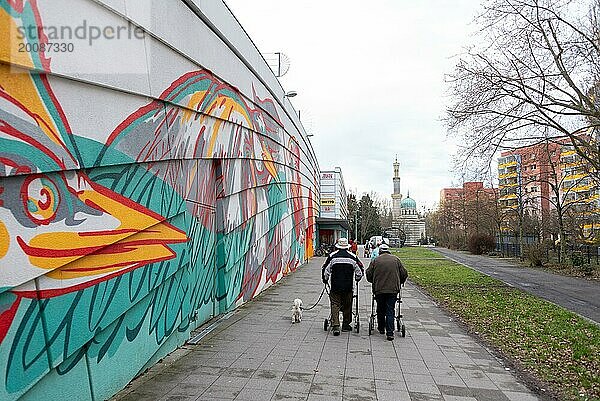 Menschen mit einem Hund laufen an einem bunten Wandgraffiti vor Wohnhäusern vorbei  dahinter Dampfmaschinenhaus in Form einer Moschee  Potsdam  Brandenburg  Deutschland  Europa