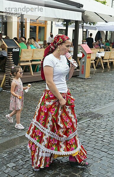 Frau in traditioneller Kleidung isst Eis auf einer belebten Straße  Kind im Hintergrund  junge Frau in Trachtenkleidung  Sibiu  Siebenbürgen  Rumänien  Europa