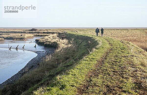 Zwei Personen  die auf der Küstenschutzmauer in der Shingle Street spazieren gehen  Suffolk  England  Großbritannien  Europa