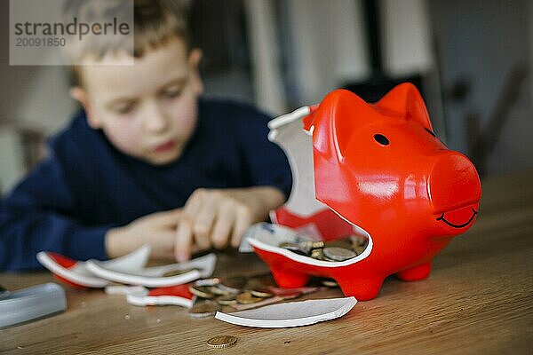 Symbolfoto zum Thema Sparen. Ein Junge zerschlägt sein Sparschein und zählt das enthaltene Geld. Berlin  10.02.2024