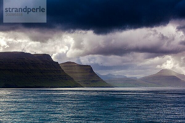 Küstenlinie der Färöer Inseln bei bedecktem und dramatischem Himmel