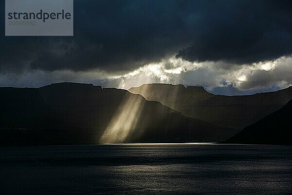 Sonnenstrahlen brechen durch dicke Wolken auf die Küstenlinie der Färöer Inseln
