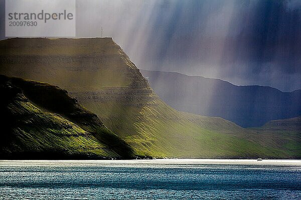 Ein Sonnenstrahl bricht durch die Wolken auf die Küste der Färöer Inseln