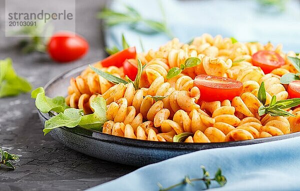 Fusilli Nudeln mit Tomatensauce  Kirschtomaten  Salat und Kräutern auf einem schwarzen Betonhintergrund. Seitenansicht  Nahaufnahme