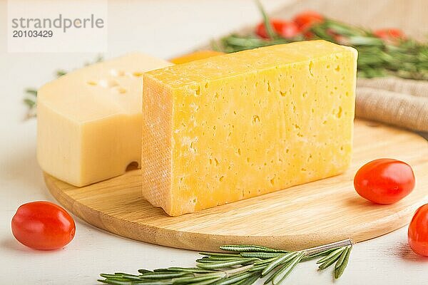 Verschiedene Käsesorten mit Rosmarin und Tomaten auf einem Holzbrett auf einem weißen Holzhintergrund und Leinenstoff. Seitenansicht  Nahaufnahme  selektiver Fokus