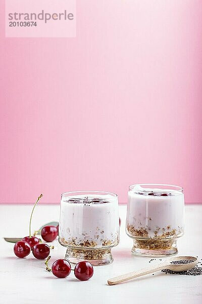 Joghurt mit Kirschen  Chiasamen und Müsli im Glas mit Holzlöffel auf rosa und weißem Hintergrund. Seitenansicht  Nahaufnahme  selektiver Fokus  Kopierraum