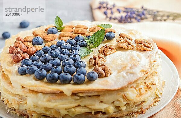 Hausgemachte geschichtete Napoleon Torte mit Milchcreme. Dekoriert mit Blaubeere  Mandeln  Walnüsse  Haselnüsse  Minze auf einem grauen Beton Hintergrund. Seitenansicht  selektiver Fokus  Nahaufnahme