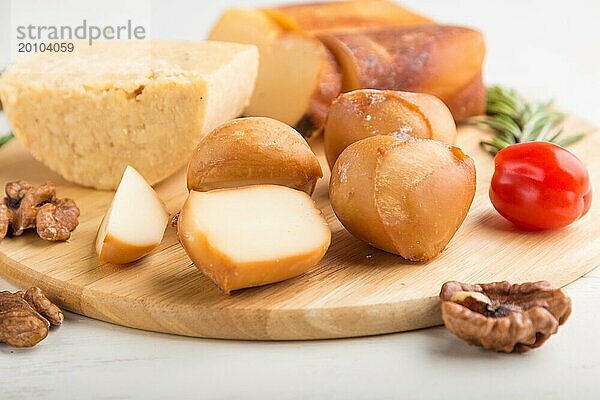 Geräucherter Käse und verschiedene Käsesorten mit Rosmarin und Tomaten auf einem Holzbrett auf einem weißen Holzhintergrund. Seitenansicht  Nahaufnahme  selektiver Fokus