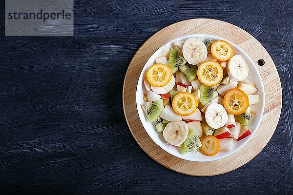 Vegetarischer Salat aus Bananen  Äpfeln  Birnen  Kumquats und Kiwi auf schwarzem woodem Hintergrund  Draufsicht  Kopierraum