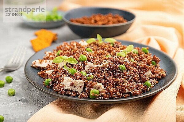 Quinoa Brei mit grünen Erbsen und Huhn auf Keramikteller auf grauem Betonhintergrund und orangefarbenem Textil. Seitenansicht  Nahaufnahme  selektiver Fokus