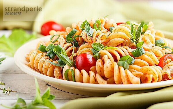 Fusilli Nudeln mit Tomatensauce  Kirschtomaten  Salat und Kräutern auf weißem Holzhintergrund mit grünem Textil. Seitenansicht  Nahaufnahme  selektiver Fokus