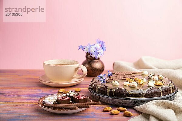 Hausgemachte Schokolade Brownie Kuchen mit Karamell Creme und Mandeln mit Tasse Kaffee auf einem farbigen und rosa Hintergrund und Leinen Textil. Seitenansicht  Kopierraum  selektiver Fokus