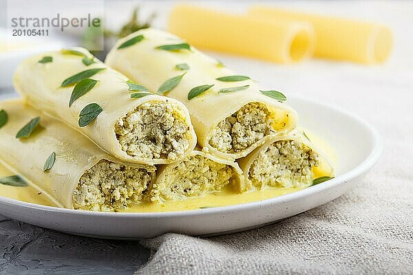 Cannelloni Nudeln mit Eiersoße  Frischkäse und Oreganoblättern auf grauem Betonhintergrund mit Leinenstoff. Seitenansicht  Nahaufnahme  selektiver Fokus