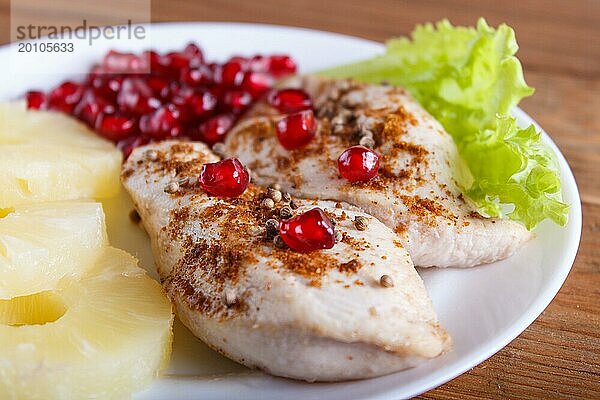 Gebratene Hähnchenfilets mit Salat  Ananas und Granatapfelkernen auf braunem Holzuntergrund  Nahaufnahme