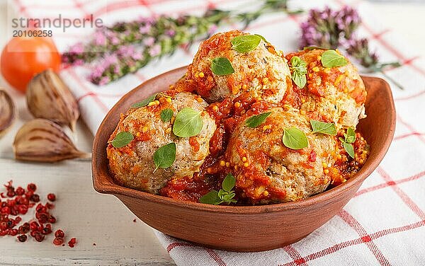 Schweinefleischbällchen mit Tomatensoße  Oreganoblättern  Gewürzen und Kräutern in einer Tonschale auf weißem Holzhintergrund mit Leinentextil. Seitenansicht  Nahaufnahme  selektiver Fokus