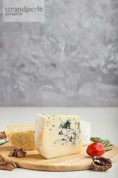 Blauschimmelkäse und verschiedene Käsesorten mit Rosmarin und Tomaten auf einem Holzbrett auf einem weißen und grauen Hintergrund. Seitenansicht  Kopierraum  selektiver Fokus