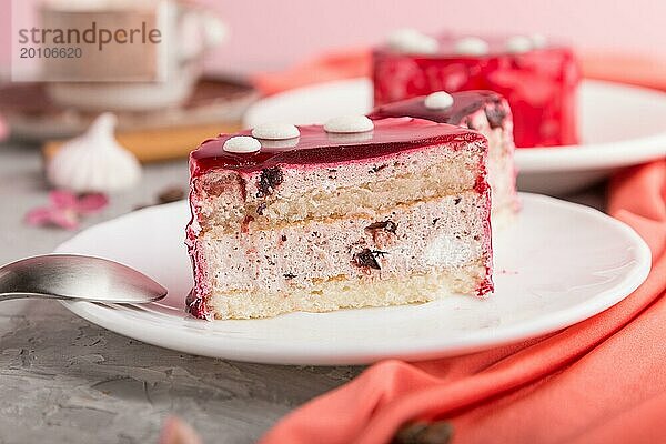 Geschnittener roter Kuchen mit Soufflé Creme und einer Tasse Kaffee auf grauem Betonhintergrund und rotem Textil. Seitenansicht  Nahaufnahme