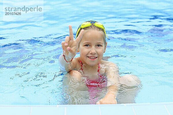 Nettes Mädchen mit Schwimmbrille im Schwimmbad zeigt Siegeszeichen