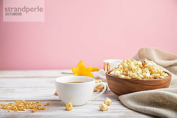 Popcorn mit Karamell in einer Holzschale und eine Tasse Kaffee auf weißem und rosa Hintergrund und Leinenstoff. Seitenansicht  Kopierraum  selektiver Fokus