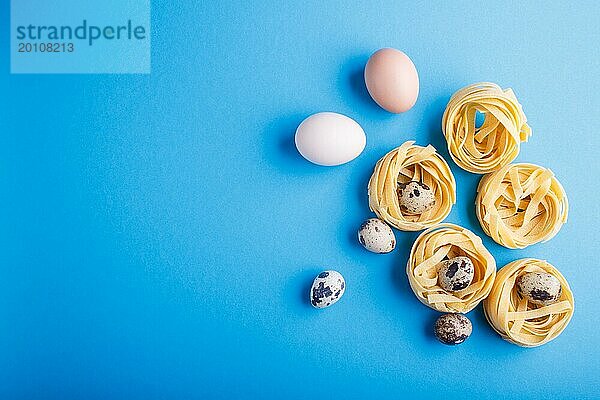 Rohe ungekochte Tagliatelle Nudeln mit Wachteleiern auf einem blauen pastellfarbenen Hintergrund. Ansicht von oben. Copy Space